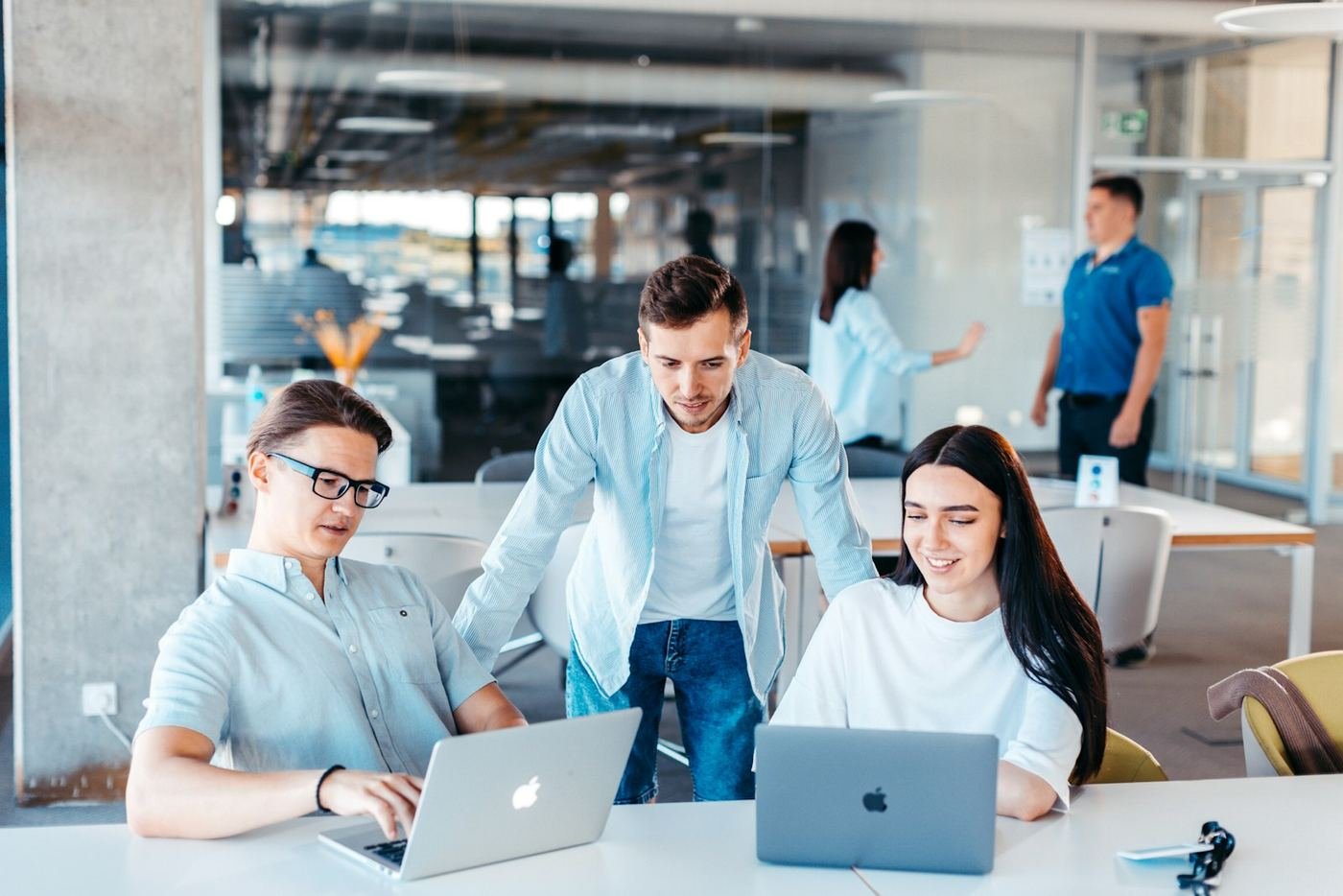 Three colleagues reviewing work together on laptops in a bright open-plan office