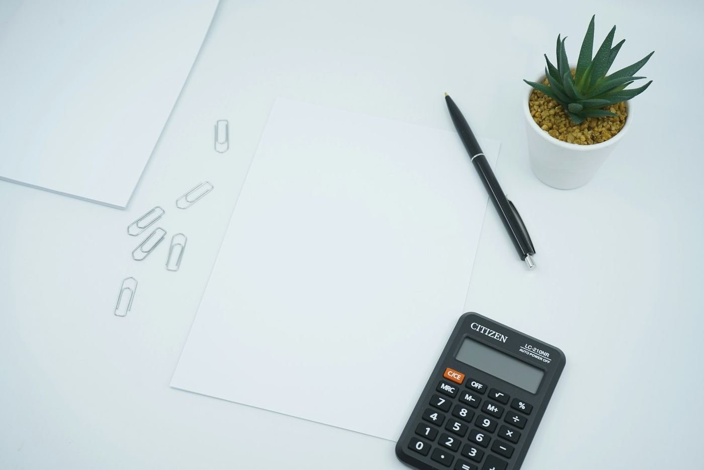 Desk calculator, pen and paper clips on a clean white desk