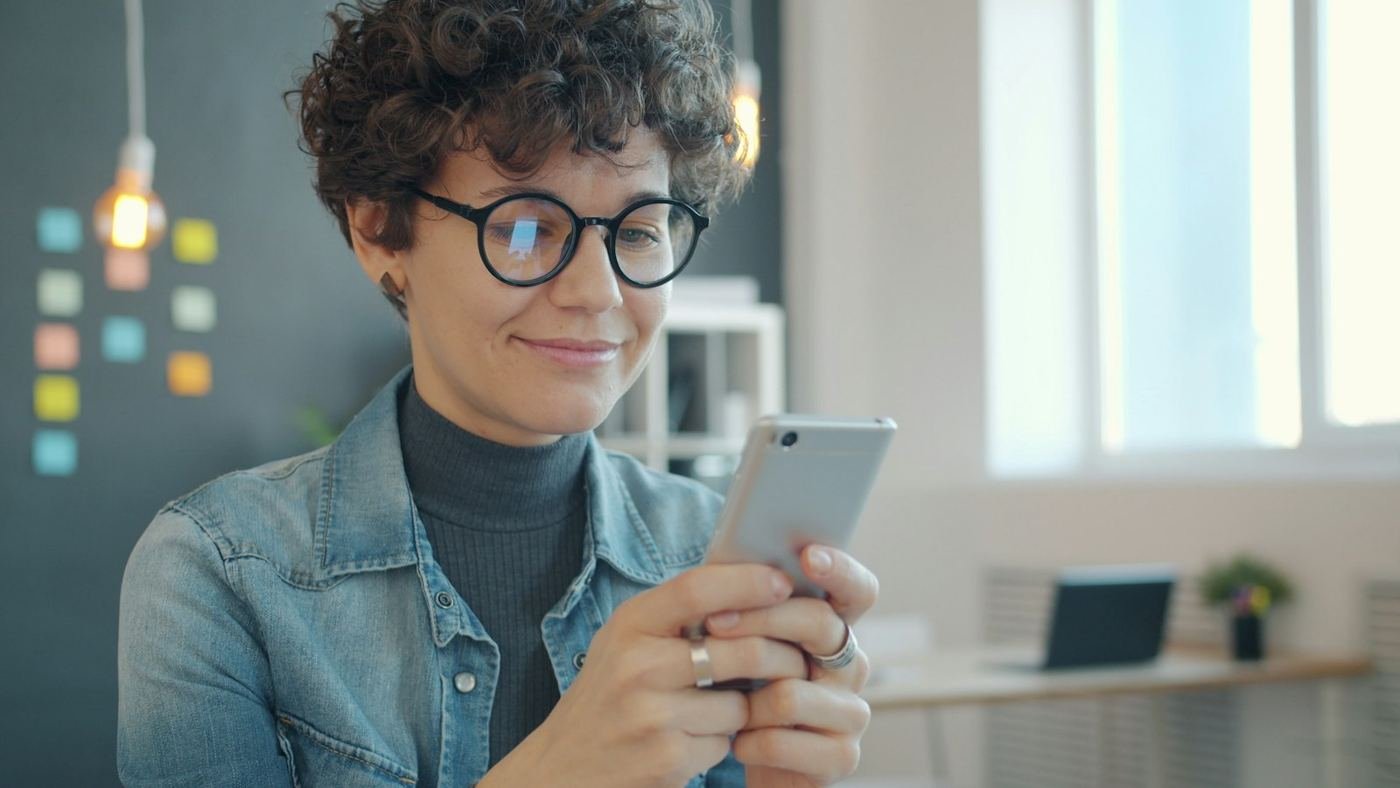 Smiling woman with glasses reading on her smartphone