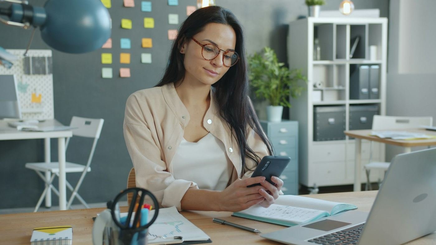 Woman at her desk checking a calculation on her phone
