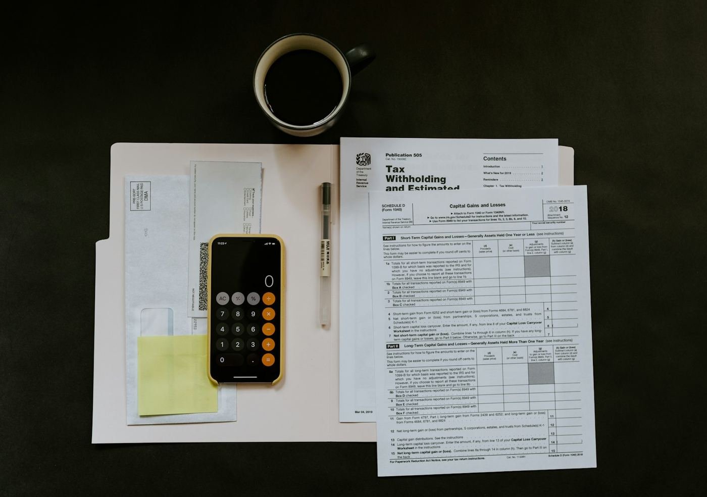 Phone calculator, coffee and US tax withholding forms on a desk